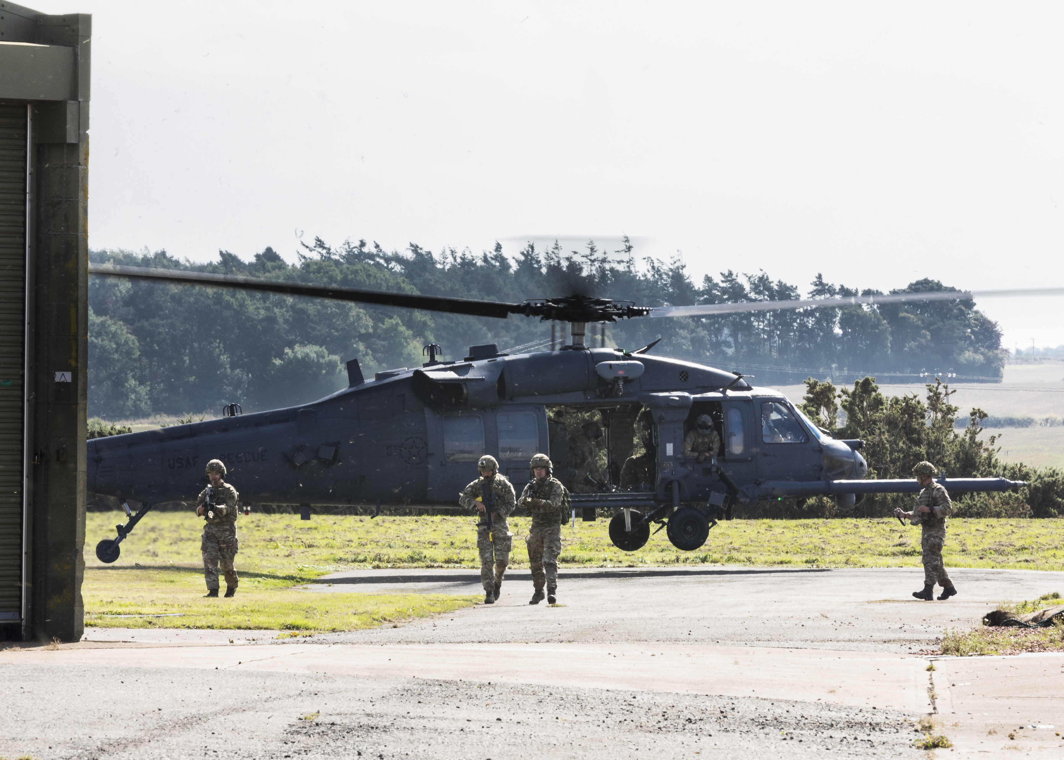Image shows RAF personnel walling with rifles, with helicopter behind.
